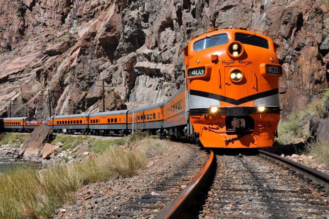 An orange train is going down the tracks near a mountain