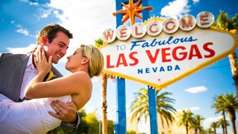 A man is holding a woman in front of a welcome to fabulous las vegas sign.