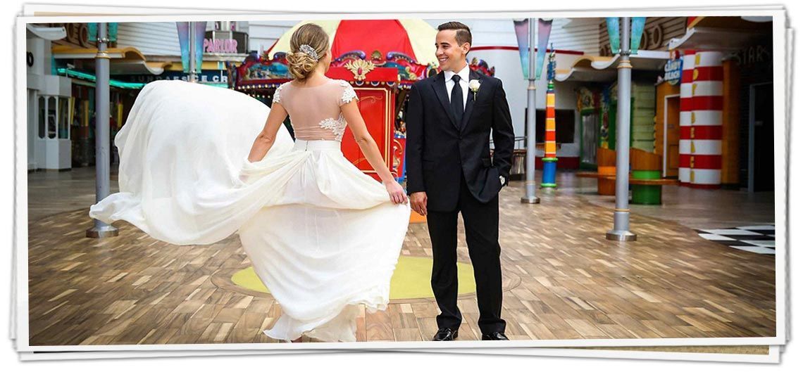 A bride and groom are standing next to each other on a wooden floor holding hands.
