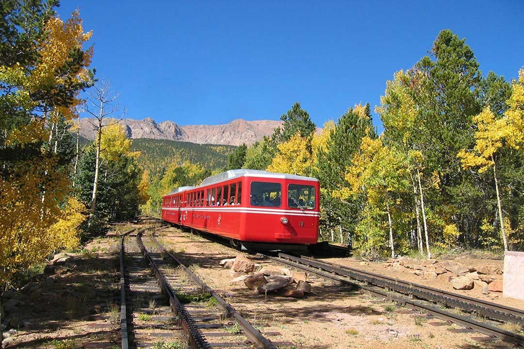 A red train is going down train tracks in the woods.