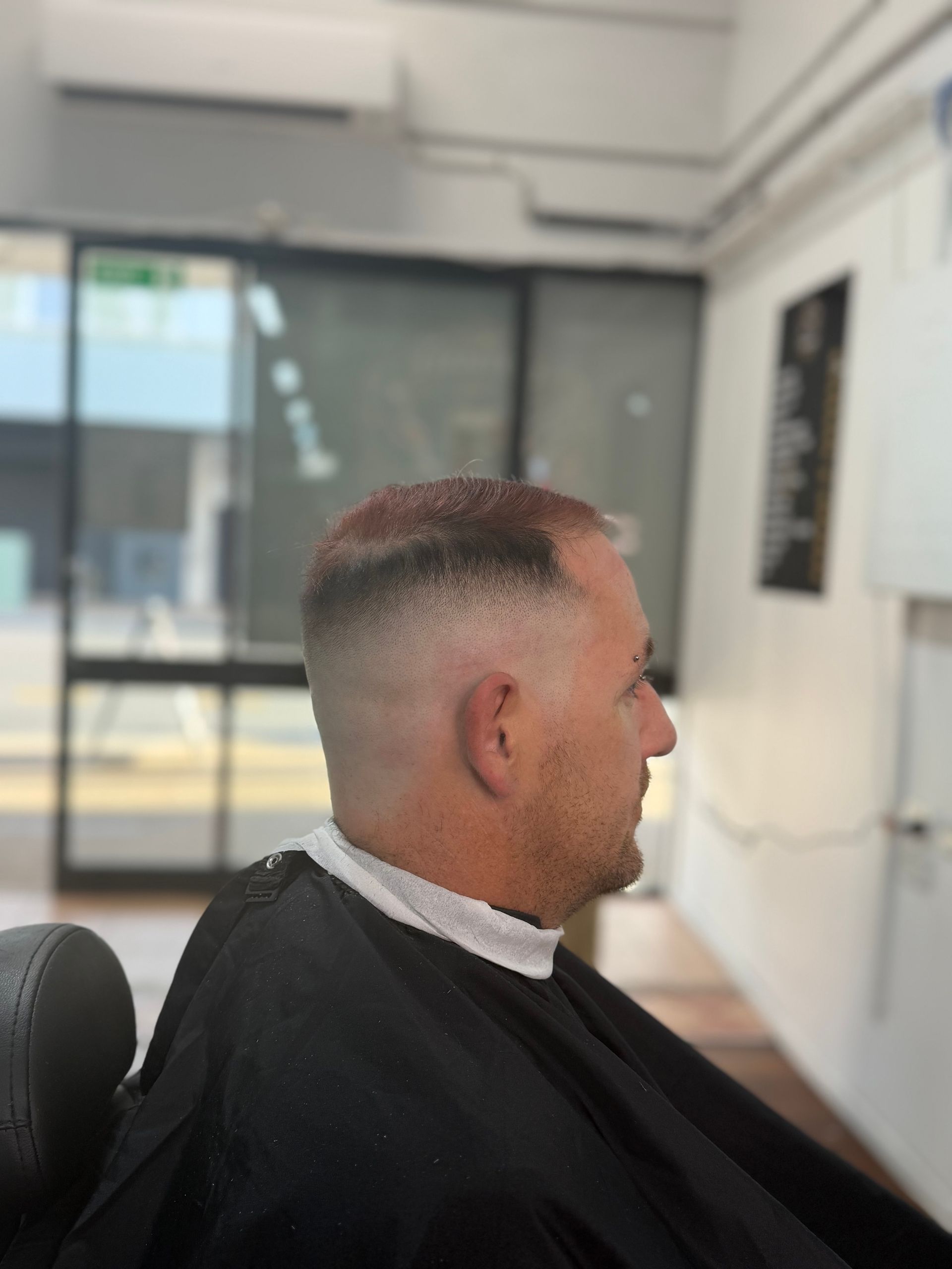 Man seated in a barber chair with a fresh fade haircut in a bright salon.