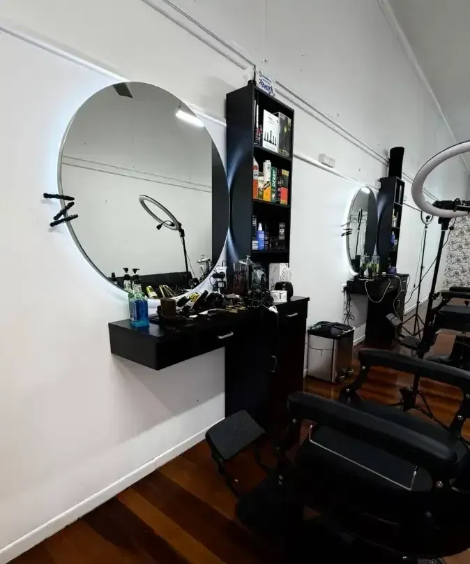 Modern salon station with round mirror, black styling counter, shelves, and a black chair on wood flooring — Ultimate Barber in Maryborough, QLD