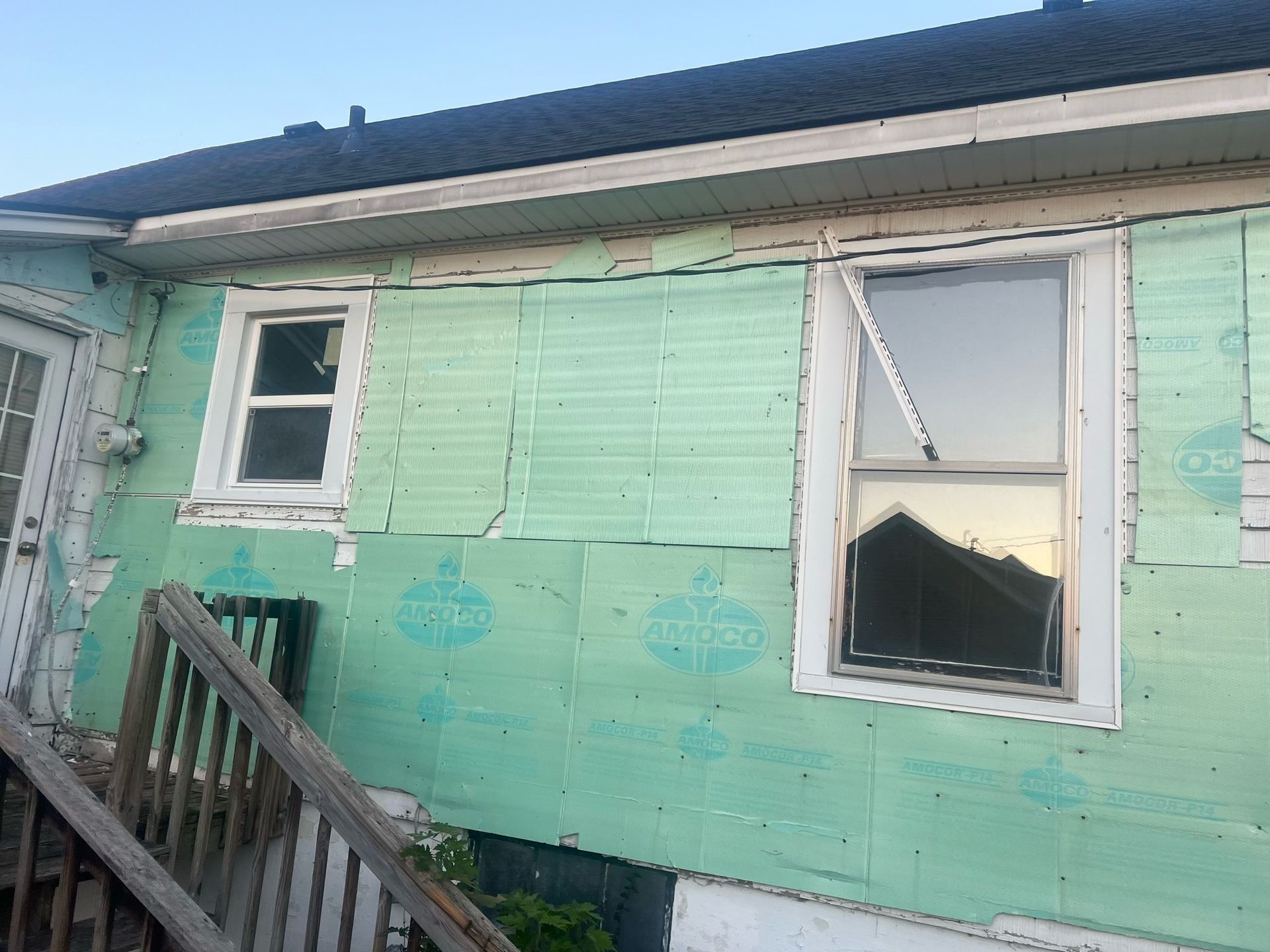 Mint-green house exterior with peeling paint, two windows, and a wooden staircase.