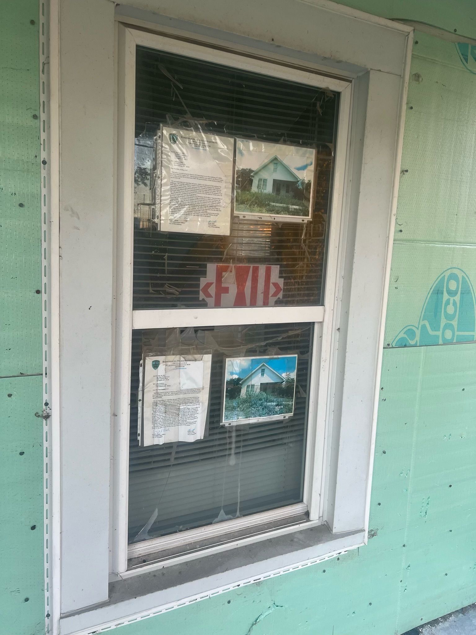 White-framed window with posted notices on a mint green wall, reflecting houses outside.