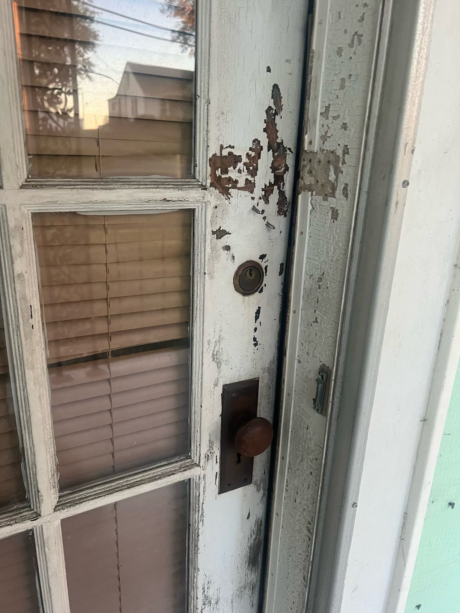 Close-up of a weathered white door with peeling paint, window panes, and a round brown doorknob.