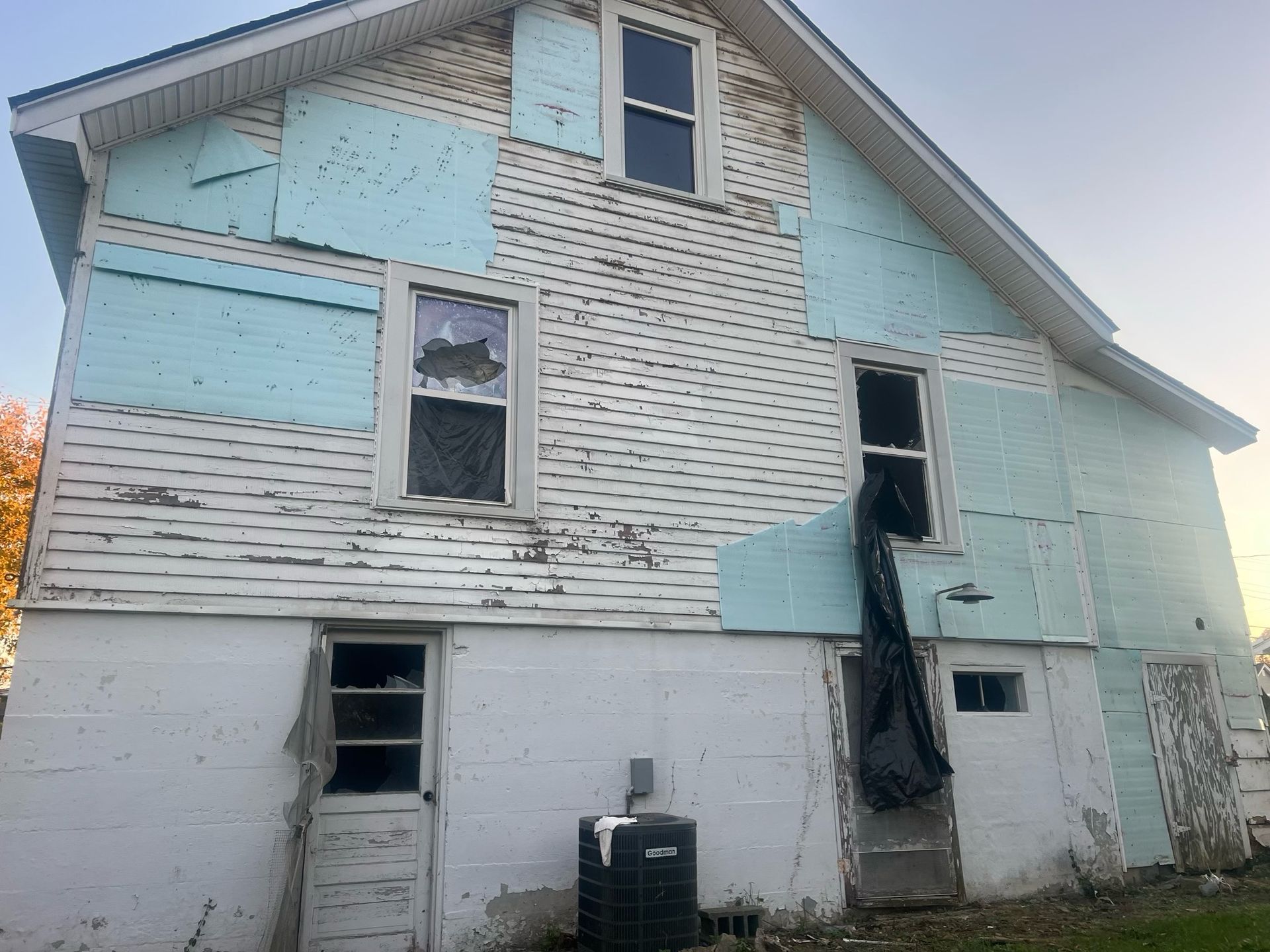 Deteriorated white house with peeling paint, broken windows, and a damaged door frame.