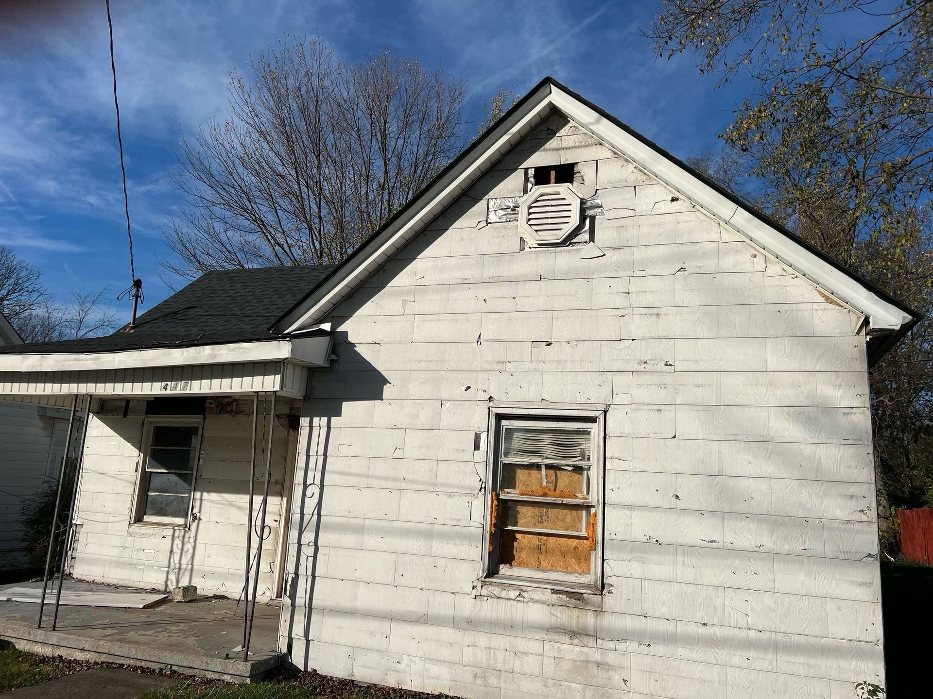 Small weathered white house with boarded window and porch under a blue sky
