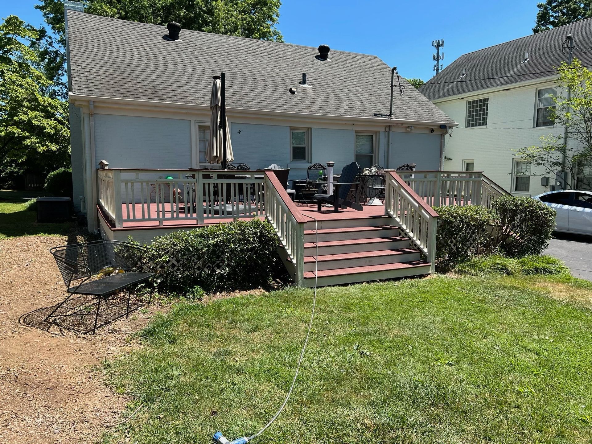 Backyard deck with stairs, chairs, and a grill beside a house, overlooking a grassy yard