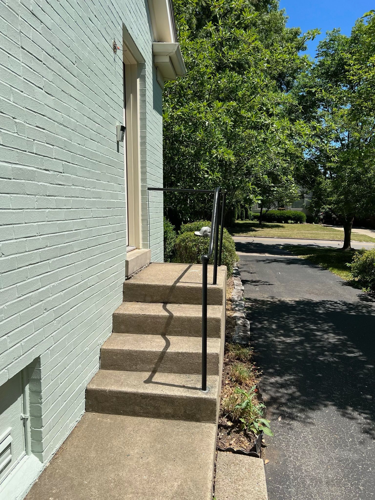Concrete steps beside a light green building, with a handrail and a tree-lined paved path beside them