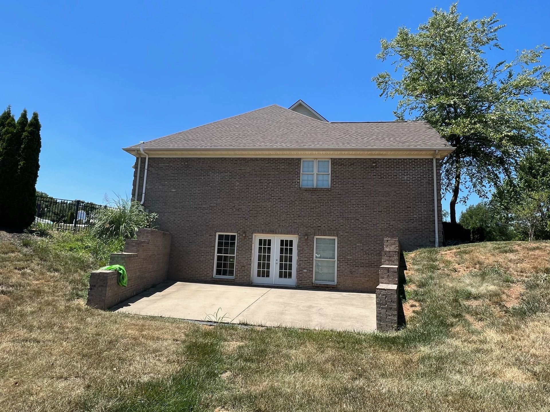 Back of a brick house with a patio and sloped yard under a clear blue sky