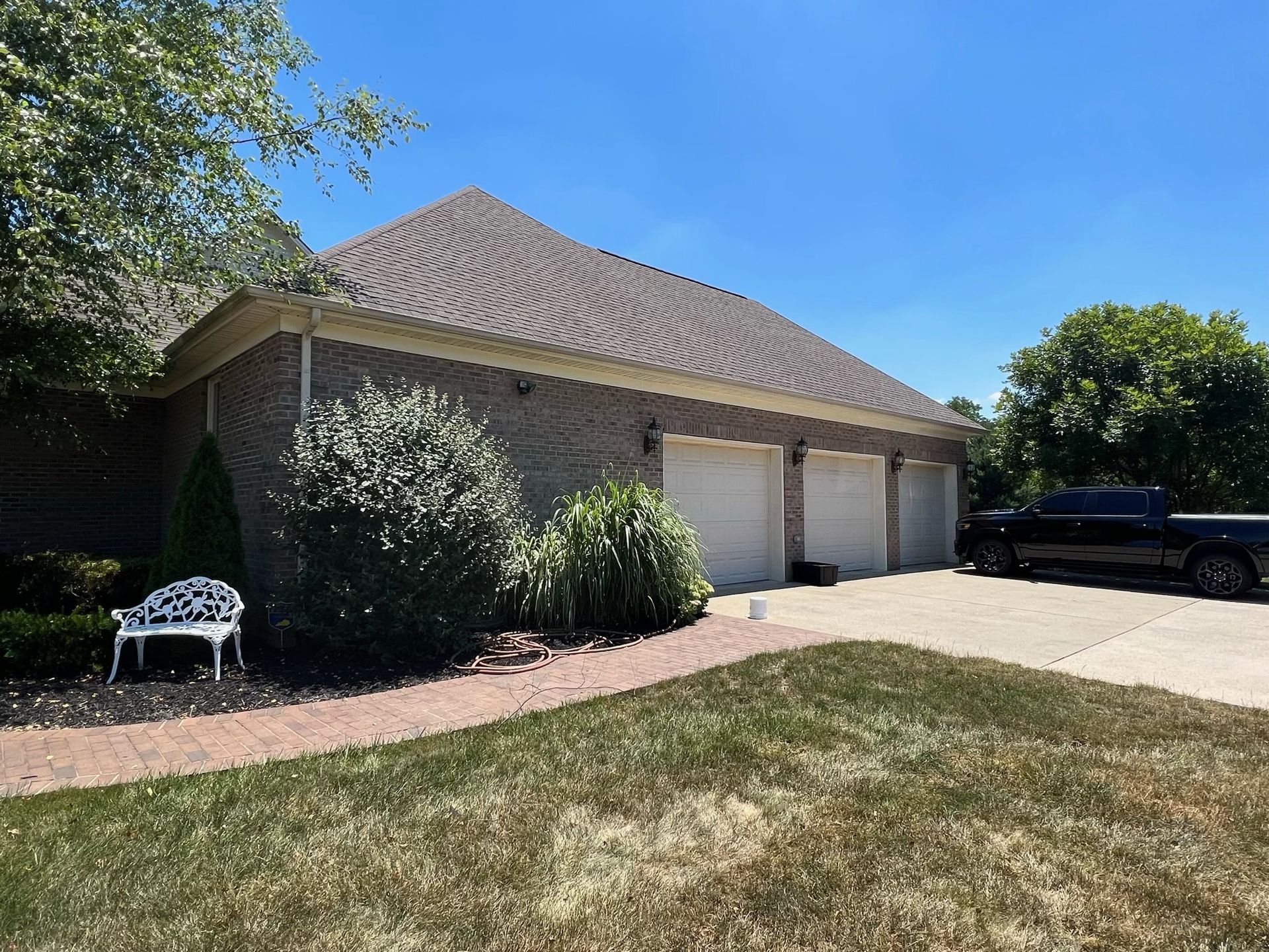 Single-story brick house with a tiled roof, two garage doors, driveway, and a parked black truck in front.