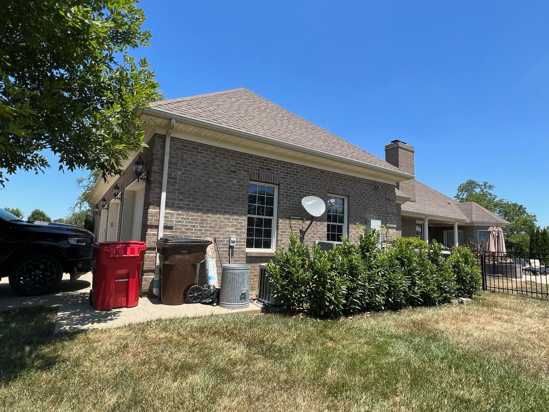 Stone house with tiled roof, front yard shrubs, and a blue sky on a sunny day