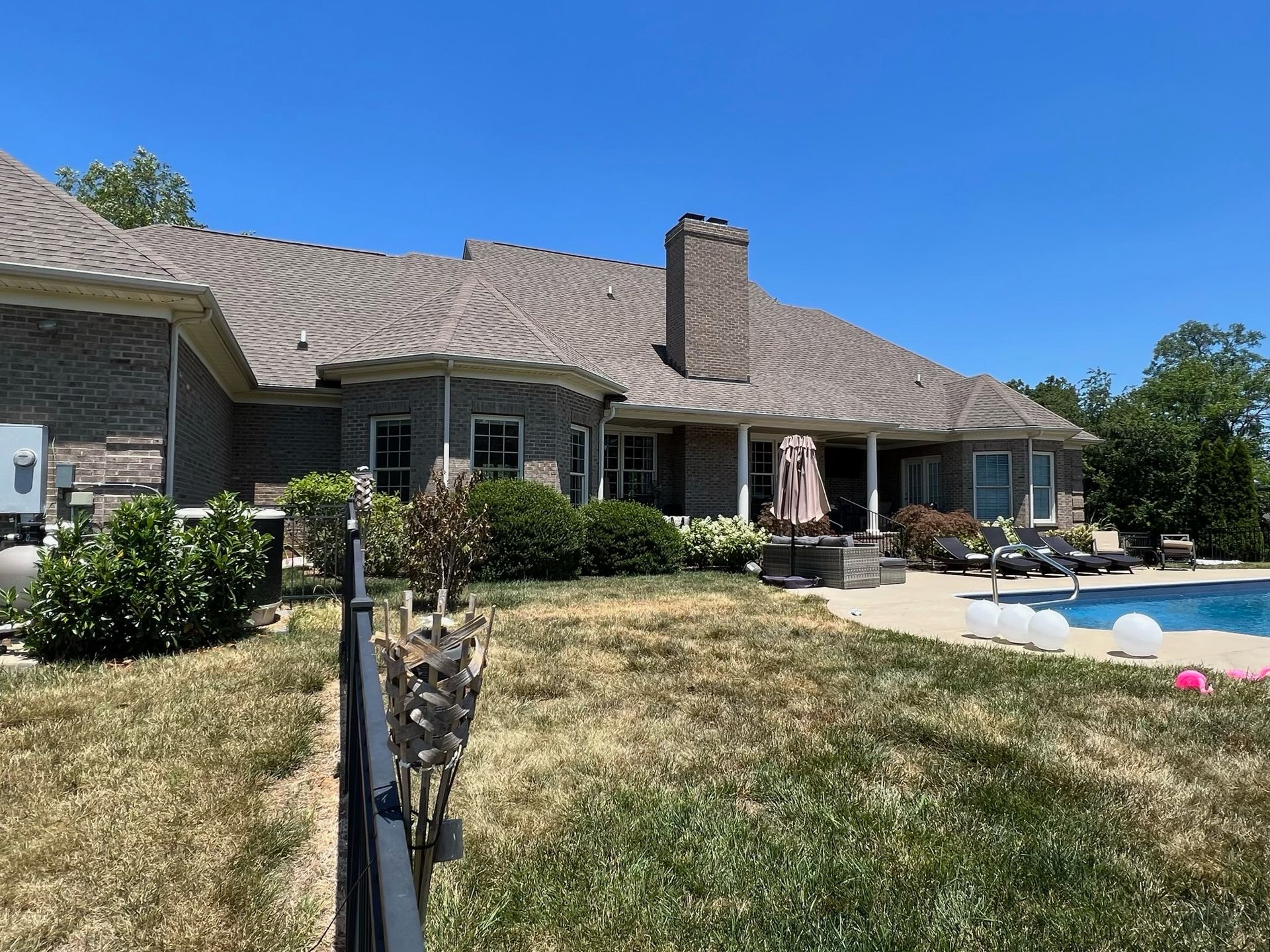 Backyard view of a single-story house with pool, patio seating, and dry grass lawn