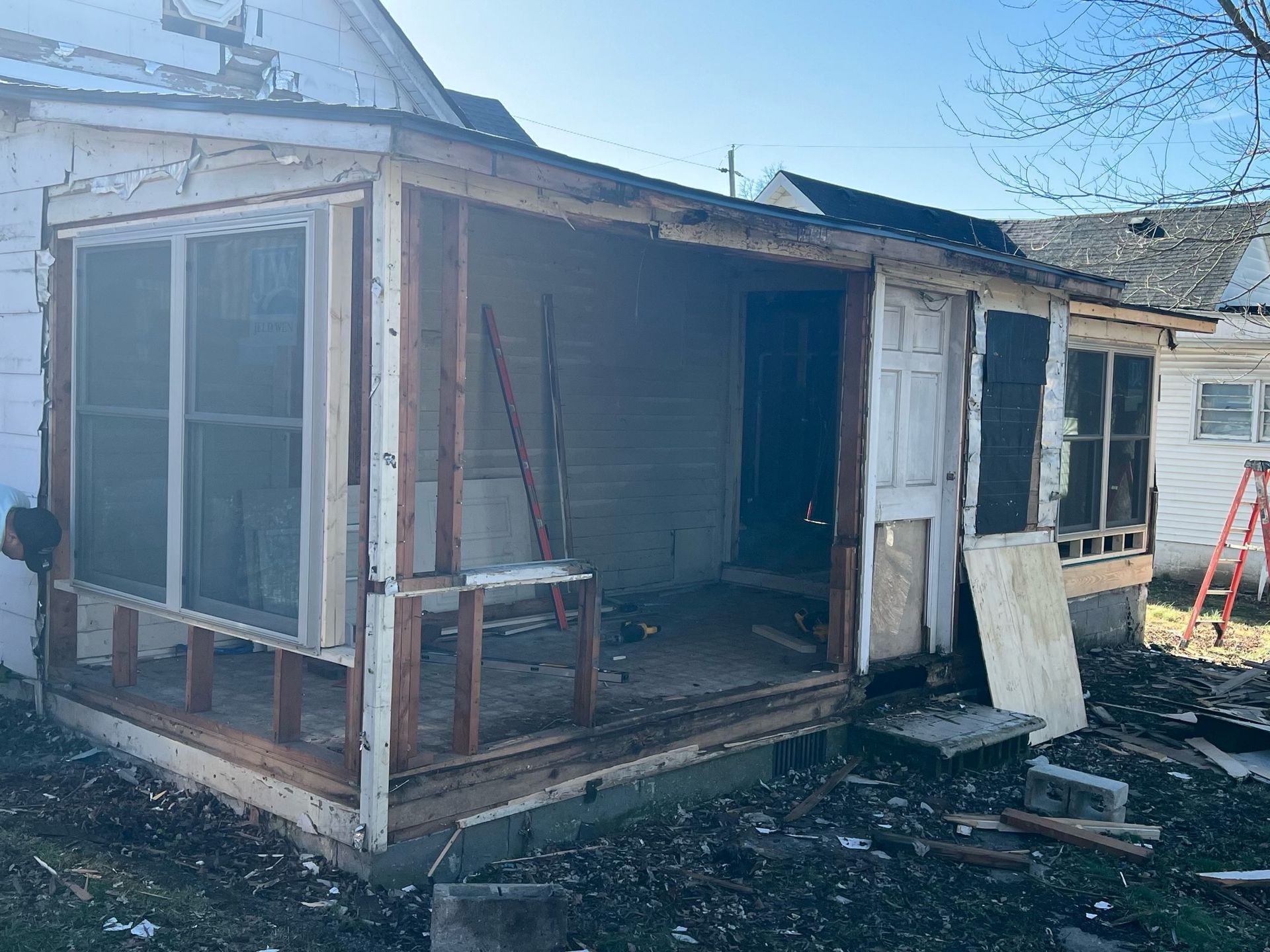 Damaged white house porch with broken windows and debris in the yard