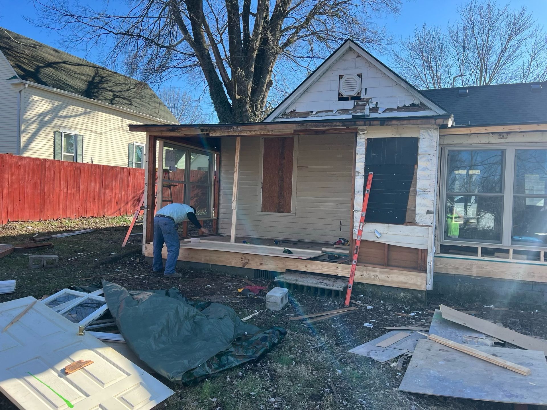 Worker renovating a small house porch with scattered building materials in the front yard