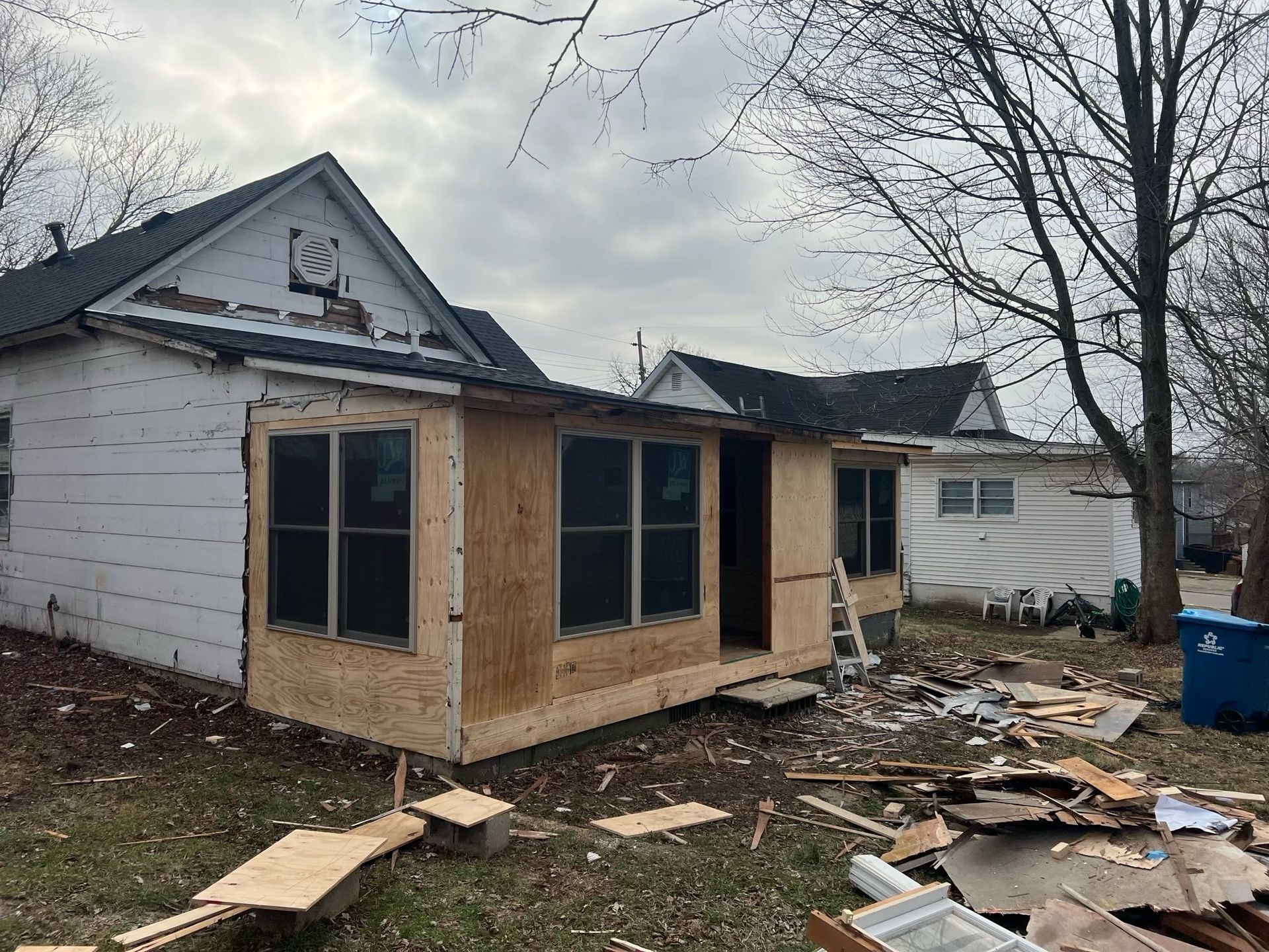 Partially rebuilt house with boarded windows and debris scattered in the yard
