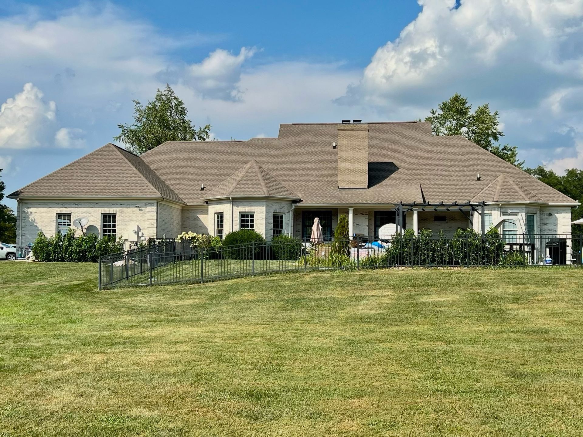 Single-story house with beige roof, fenced patio, and large grassy lawn under a blue sky