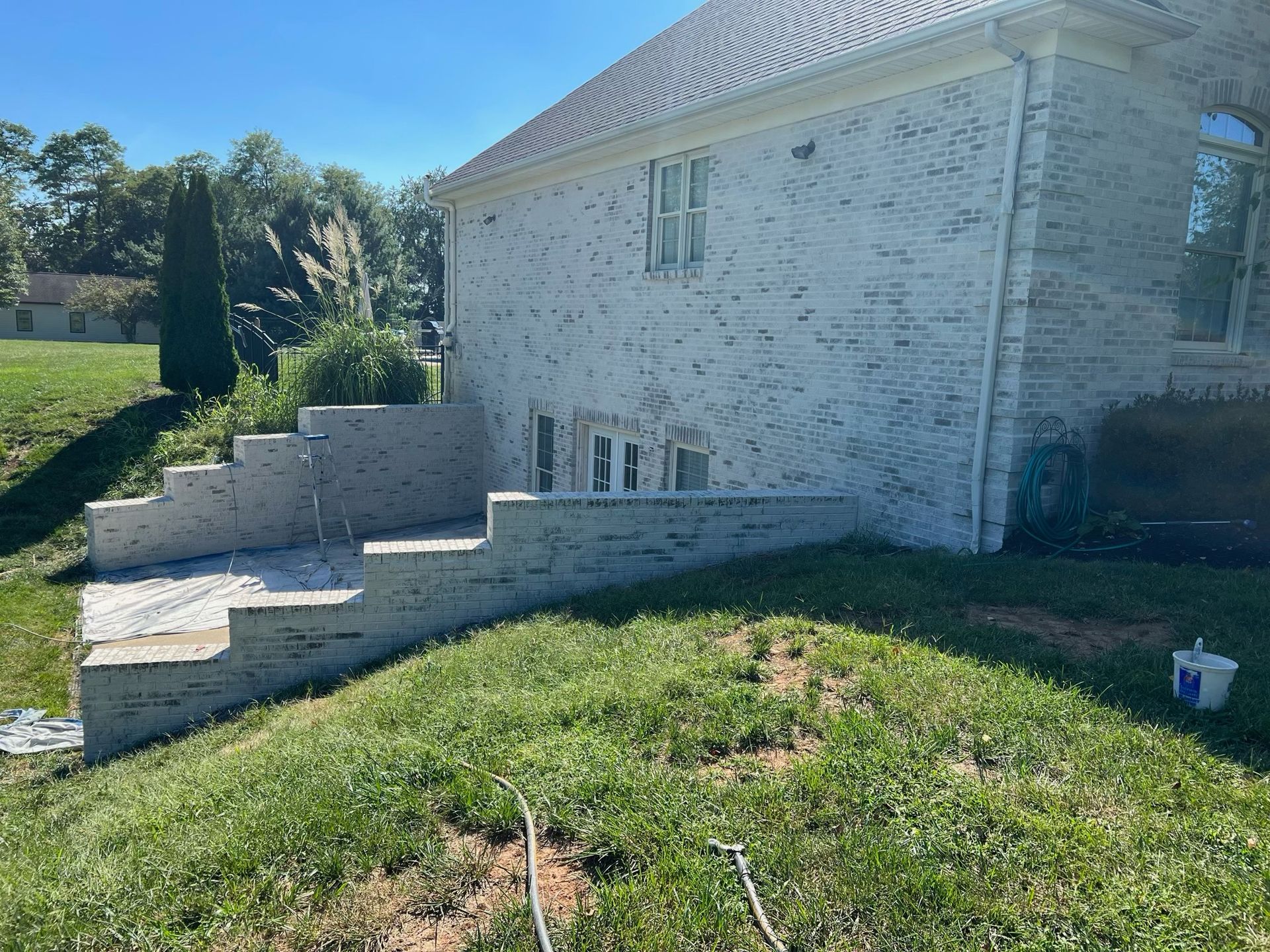 White house with stone steps and a sloped grassy yard in bright sunlight