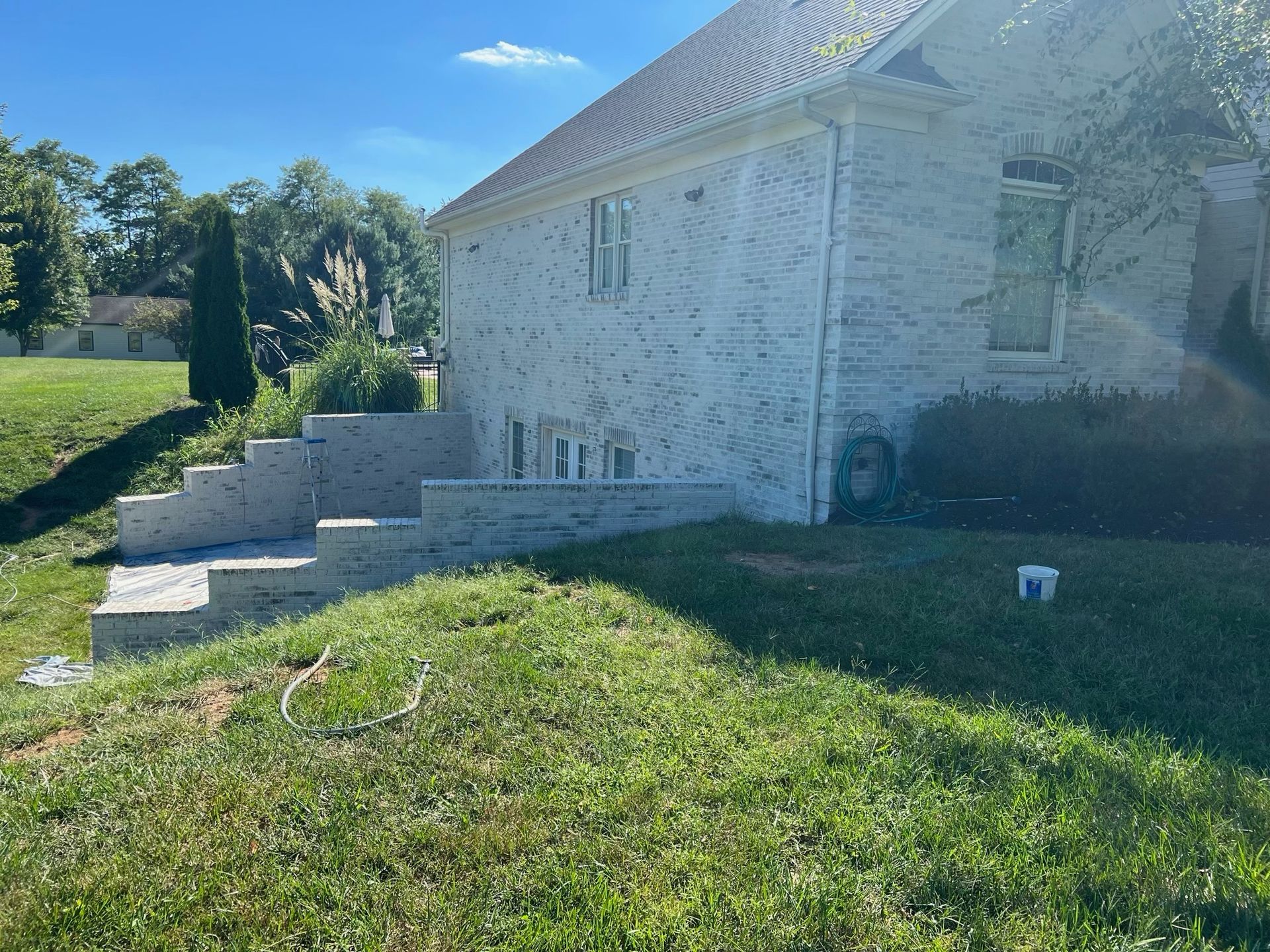 Stone house with a sloped roof beside a grassy yard and concrete steps on a sunny day