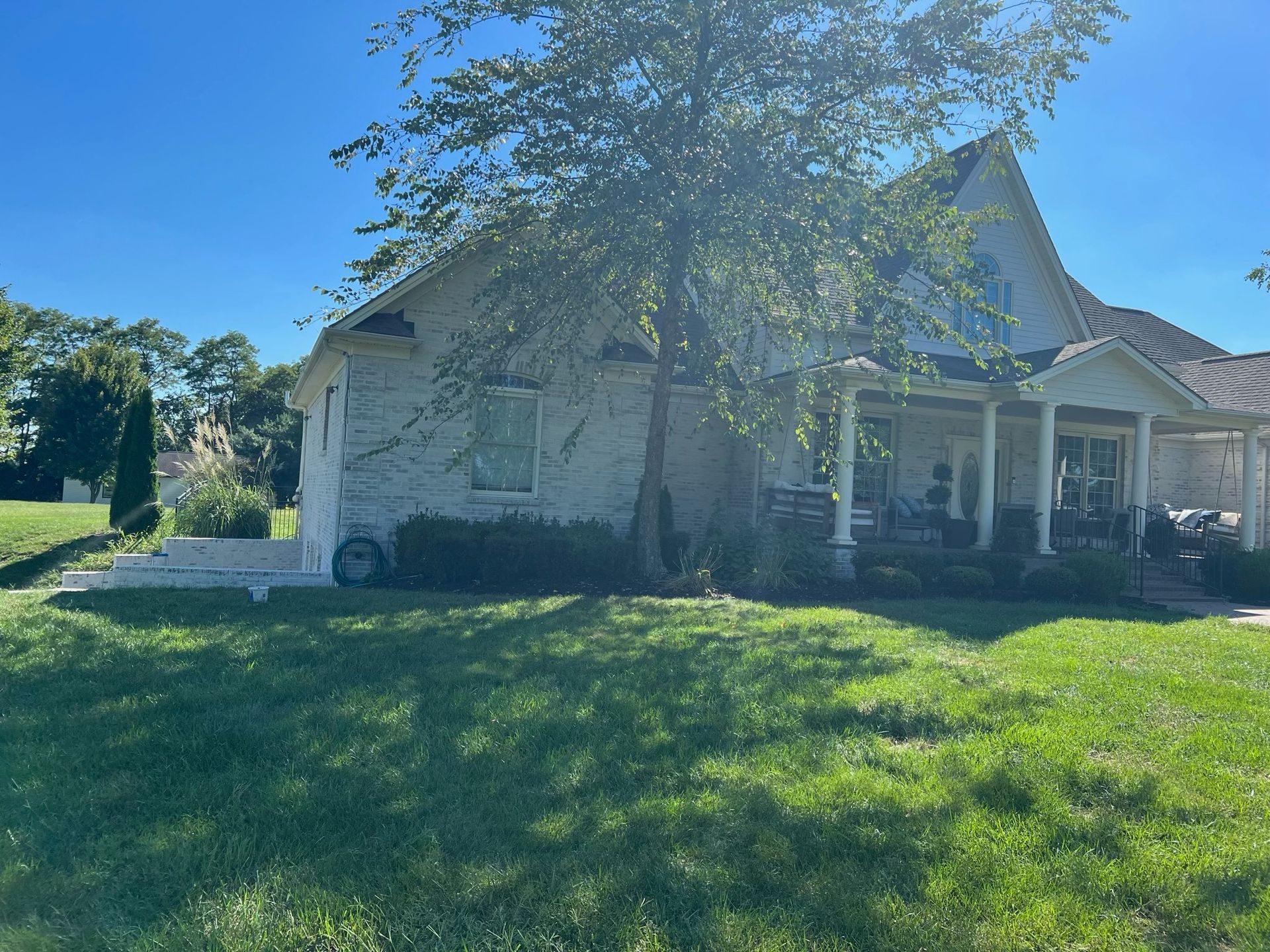 White house with a front porch and large tree in a sunny grassy yard