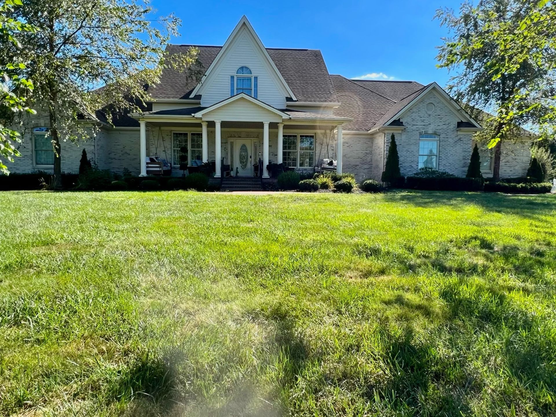 Large white suburban house with a front porch and a wide green lawn under a blue sky