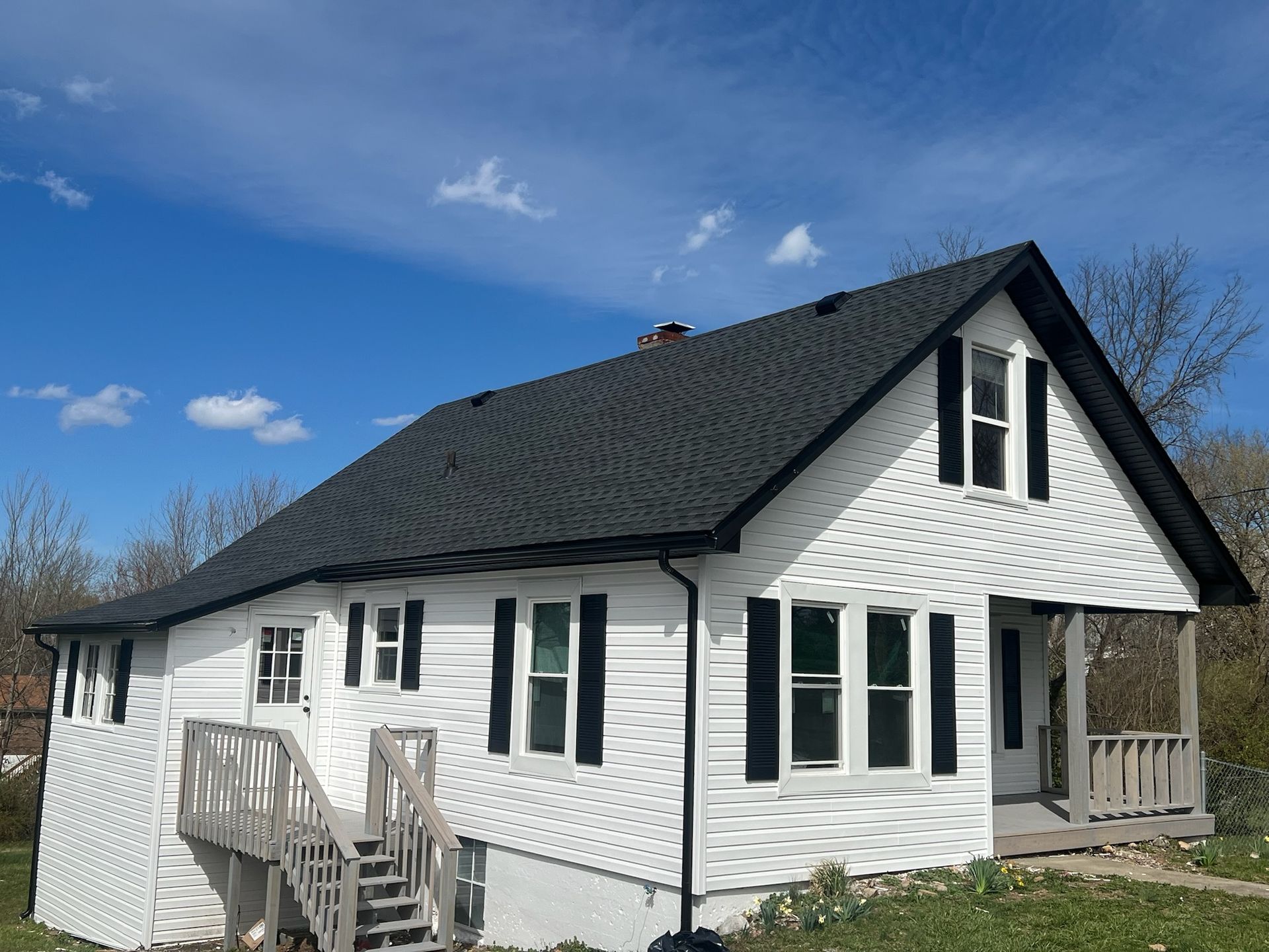 White house with black roof and small porch under a blue sky