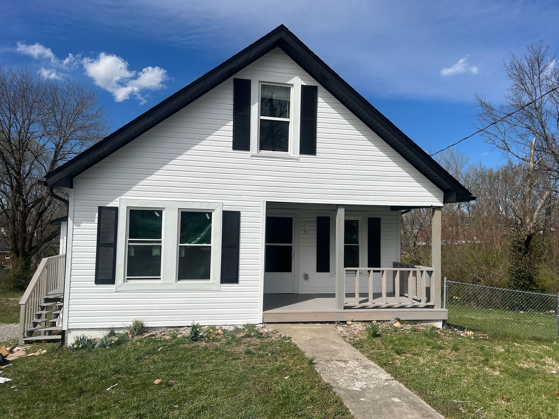 White house with dark shutters and front porch under a blue sky, viewed from the yard