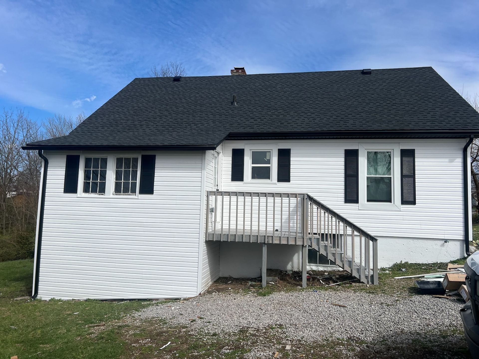 White house with black roof and small front porch on a gravel lot under a blue sky