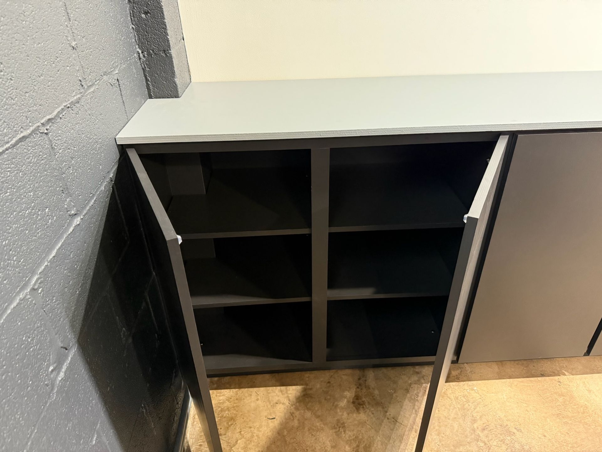Black cubby cabinet with open doors in a hallway corner, showing empty shelves.