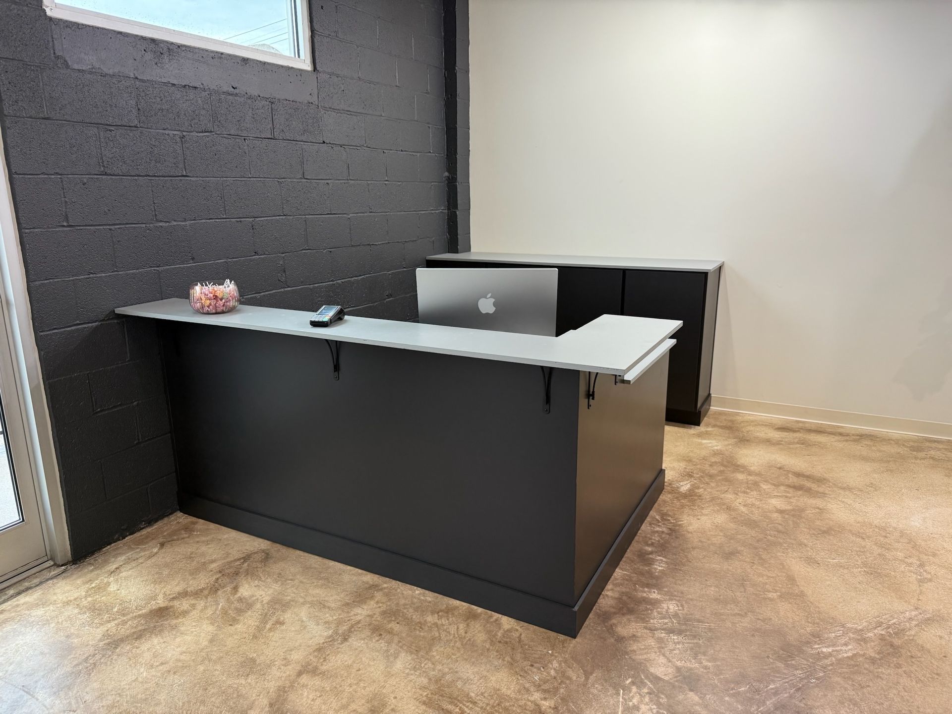 Empty office reception desk with a laptop, black walls, and tan carpeted floor