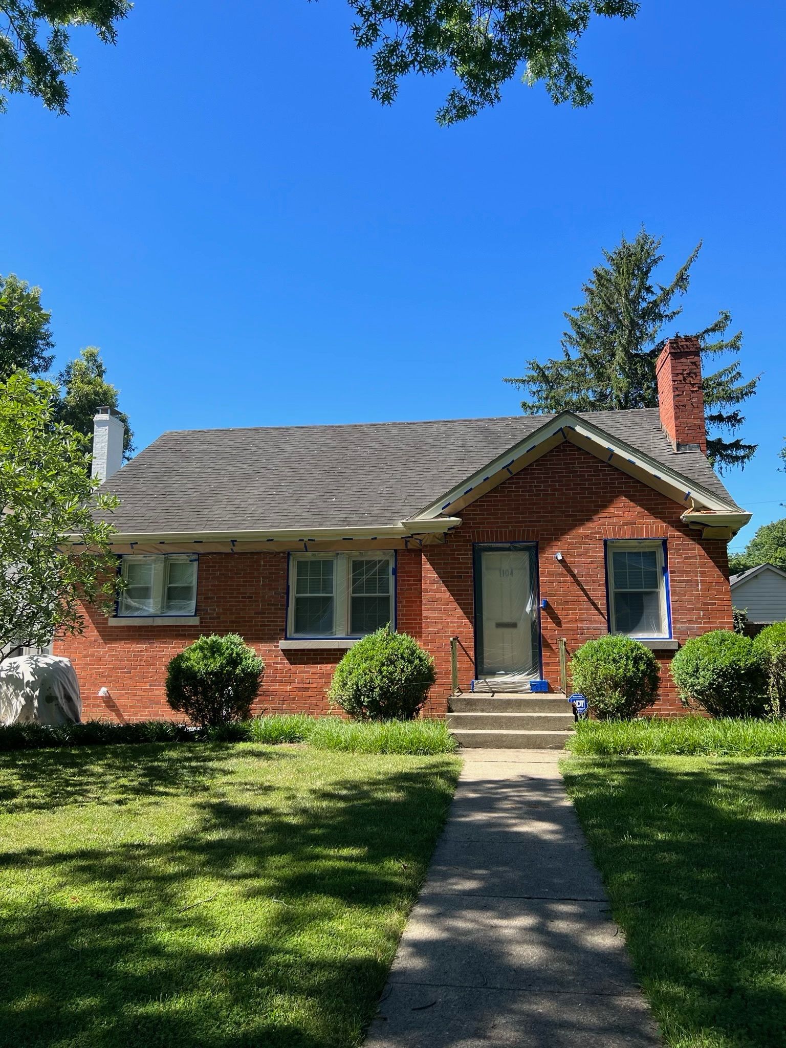 Brick house with front walkway, green lawn, and blue sky on a sunny day