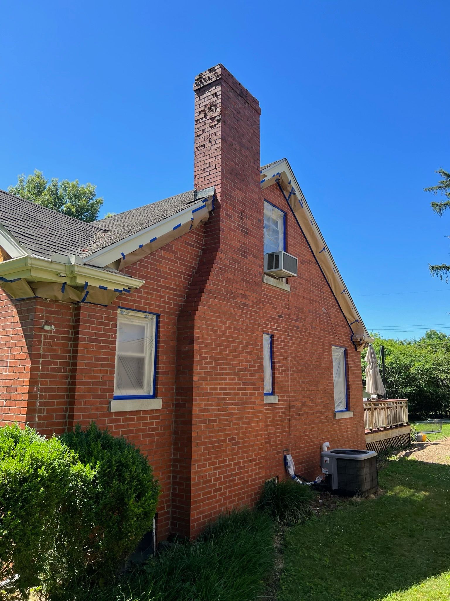 Red brick house exterior with a tall chimney and small windows under a clear blue sky