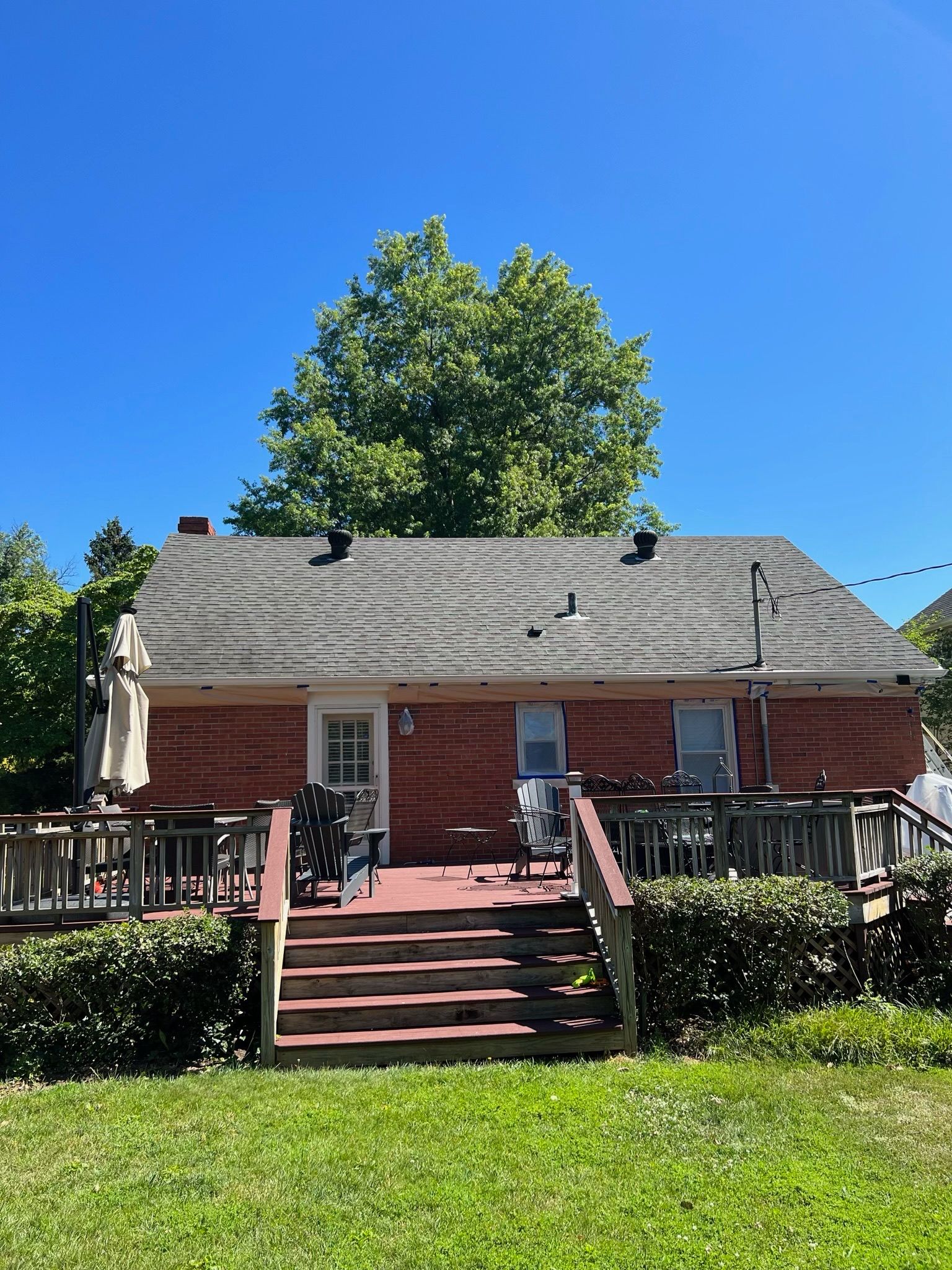 Brick house with front porch, red steps, and green lawn under a blue sky