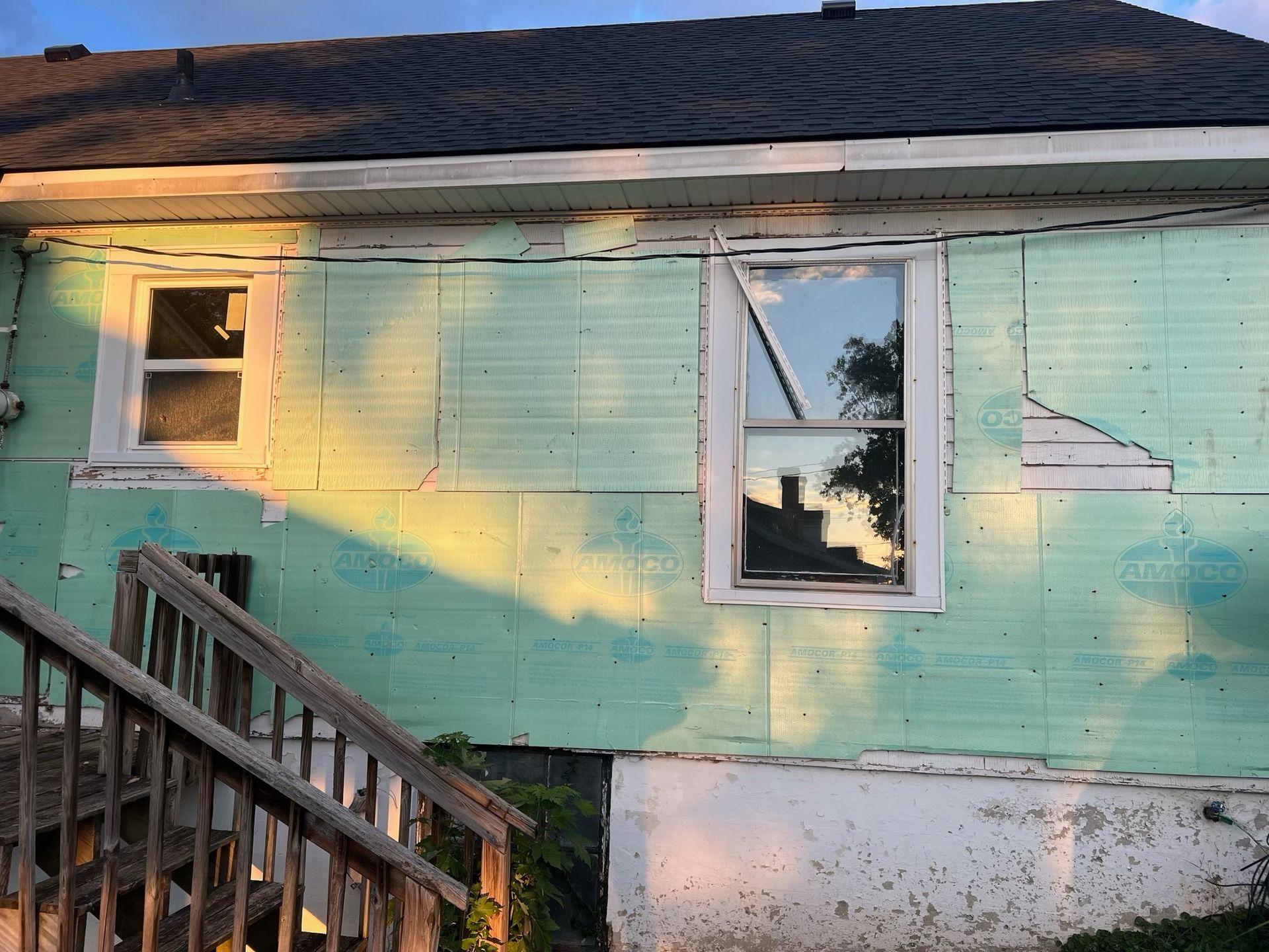 Mint-green house exterior with broken windows, peeling paint, and a wooden porch railing at sunset.
