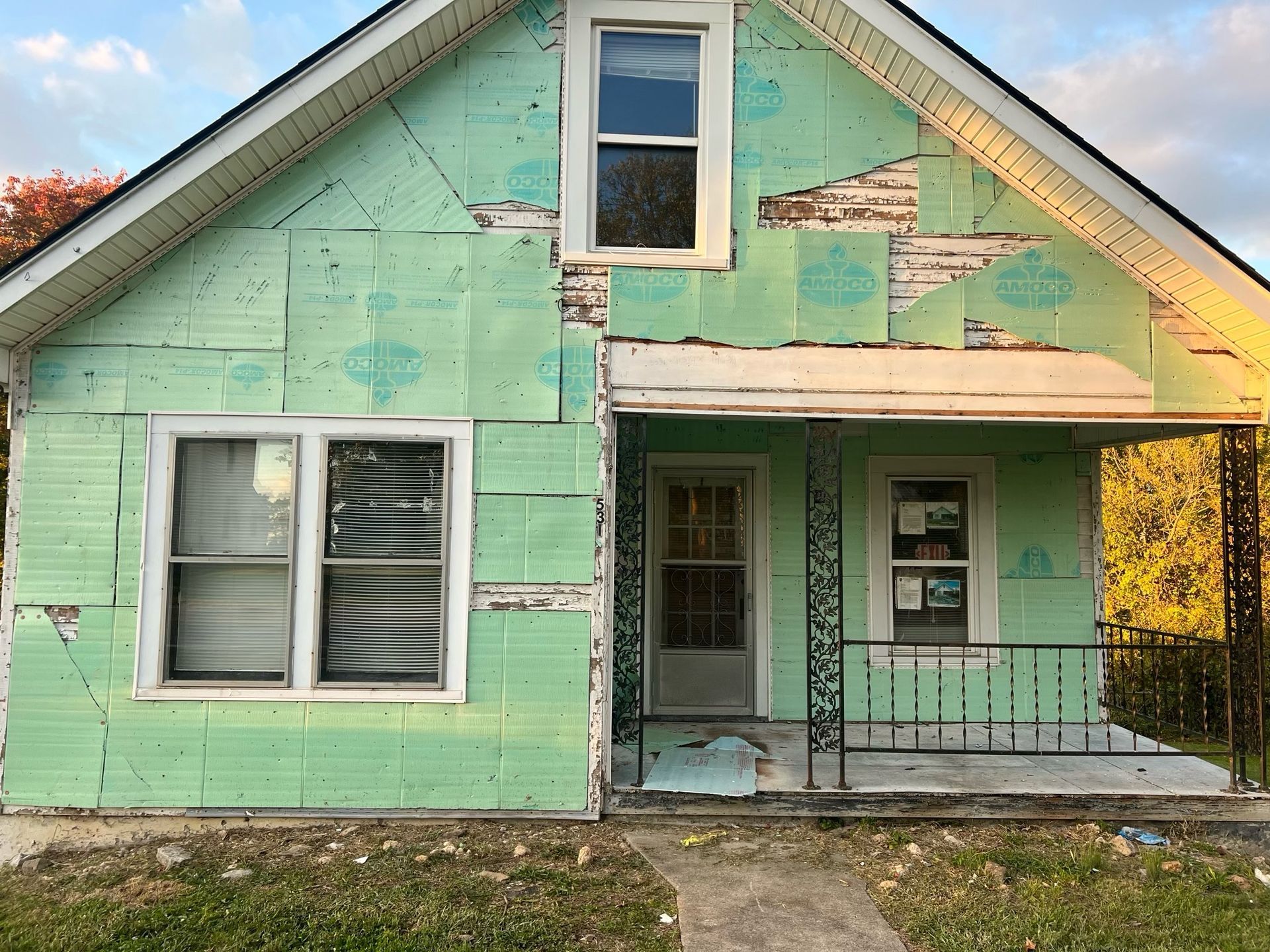 Weathered mint-green house with a small front porch and peeling paint.