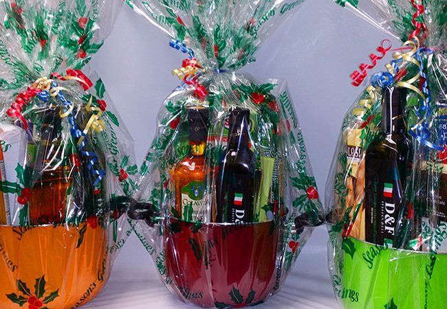 Three gift baskets are wrapped in plastic and one of them has a bottle of d & f on it