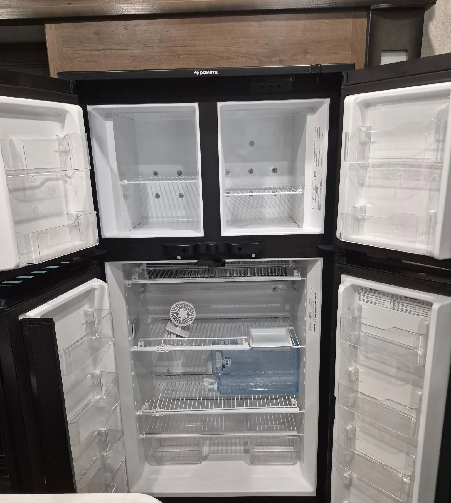 Open refrigerator with empty shelves, white doors, and a black exterior in a kitchen.