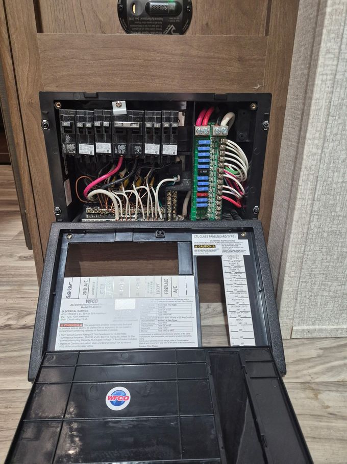 Technician wiring an electrical panel inside a wooden cabinet with pipes and blue tank components