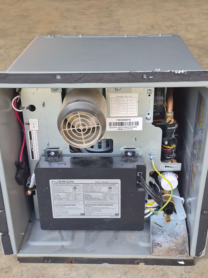 Person repairing wiring inside a recreational vehicle kitchen cabinet while a tool bag rests nearby
