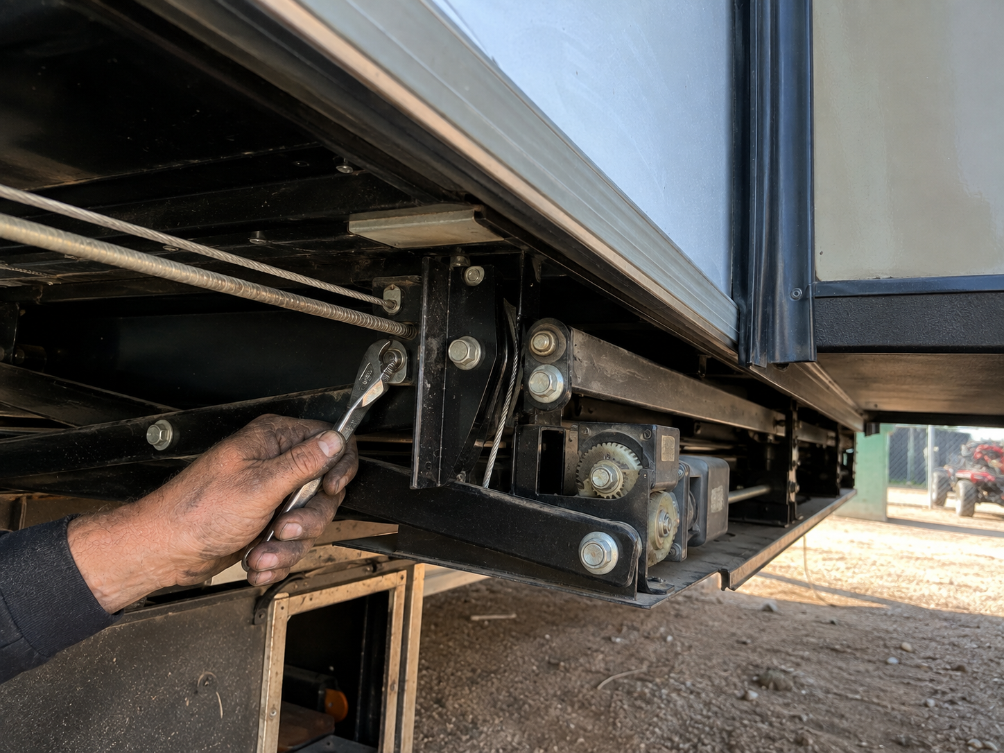Hand using a wrench to tighten a black metal bracket under a trailer or truck bed