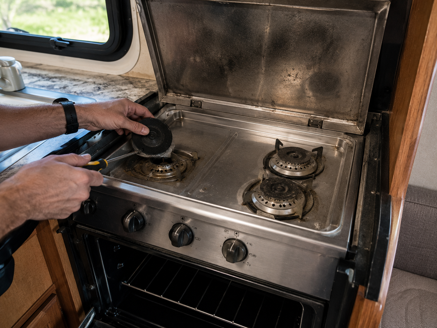 Person cleaning a stainless steel gas stove in an RV kitchen.