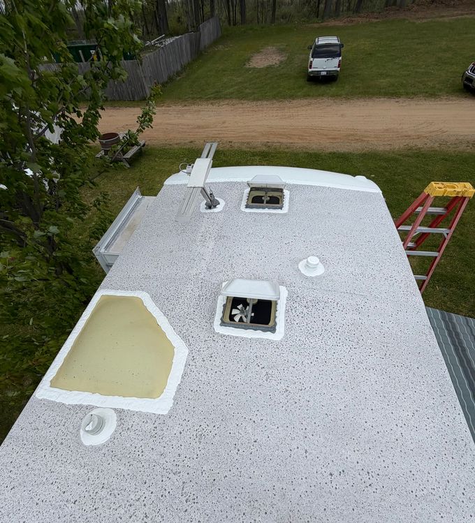 Worker removing damaged roofing on a flat roof, with exposed plywood and tools scattered nearby