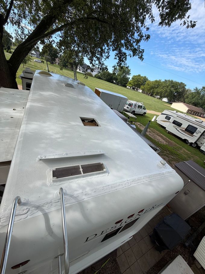 Person painting a white RV roof with a roller beside a paint bucket