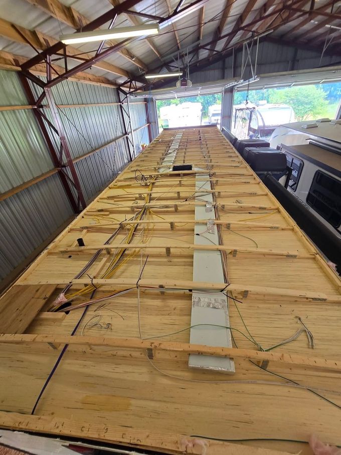 Roof under repair with exposed plywood and a worker rolling out black roofing material