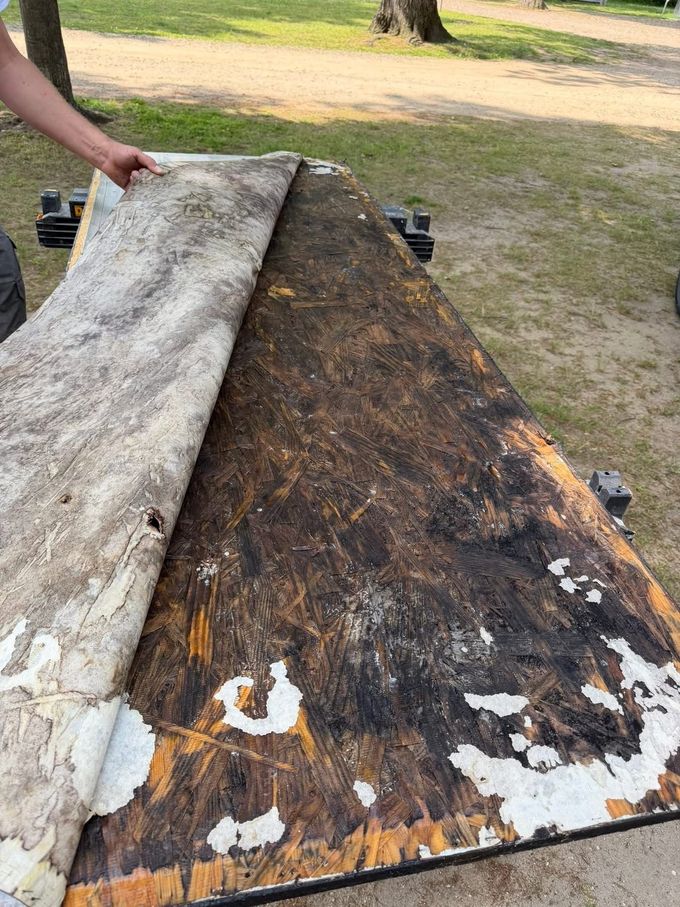 Damaged wooden RV step and porch area with a loose mat on gravel near the doorway