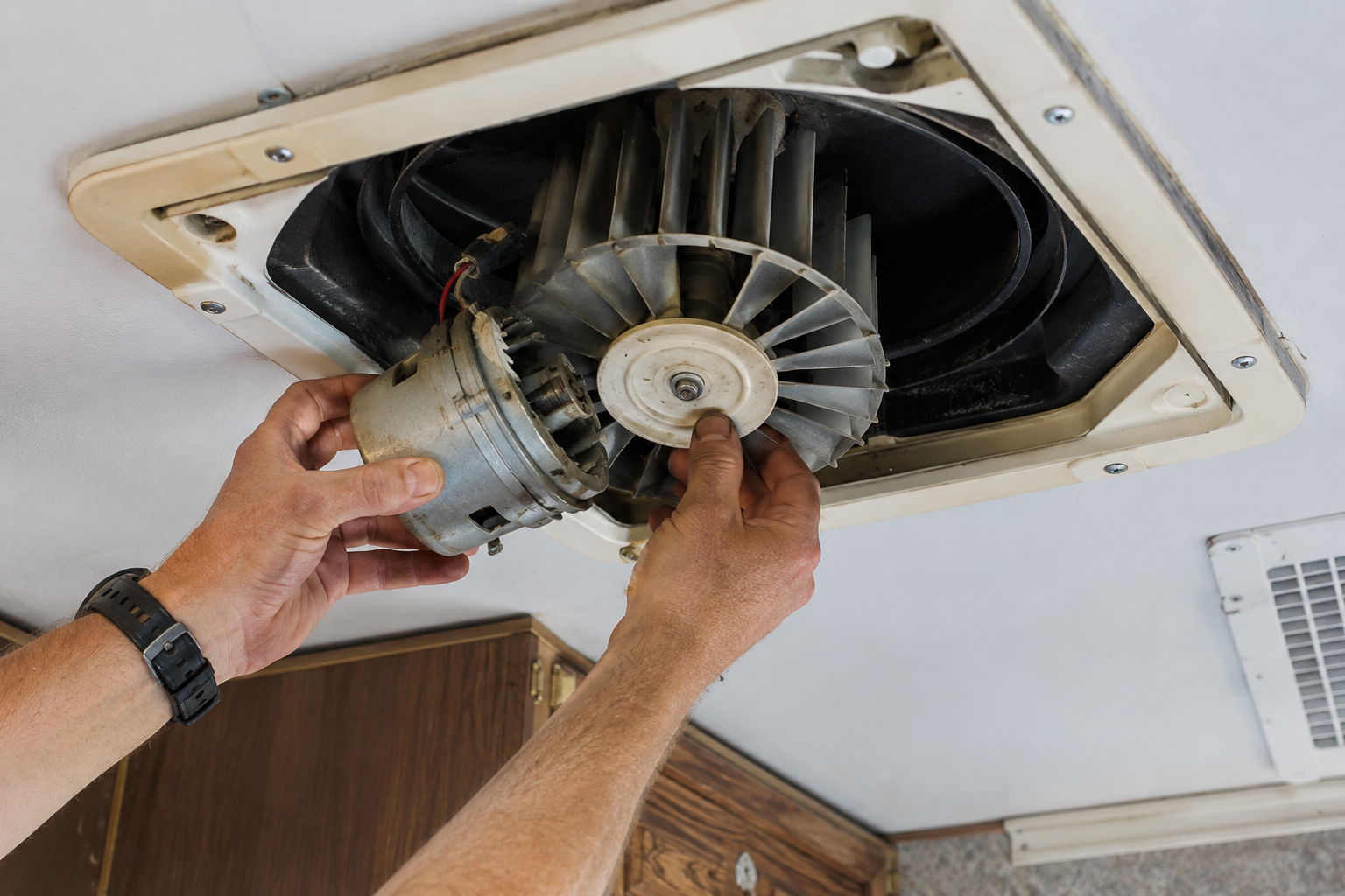 Hands installing a ventilation fan in a ceiling opening with exposed ducting.