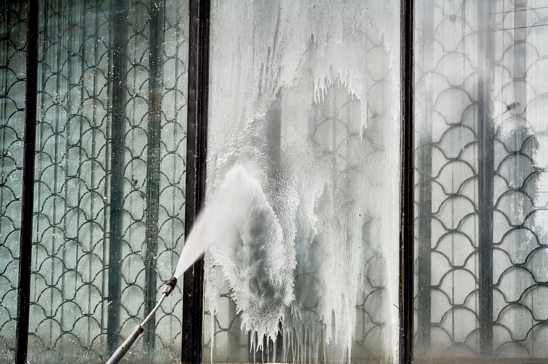 Person spraying a white substance onto a patterned metal gate, leaving a foamy streak and residue