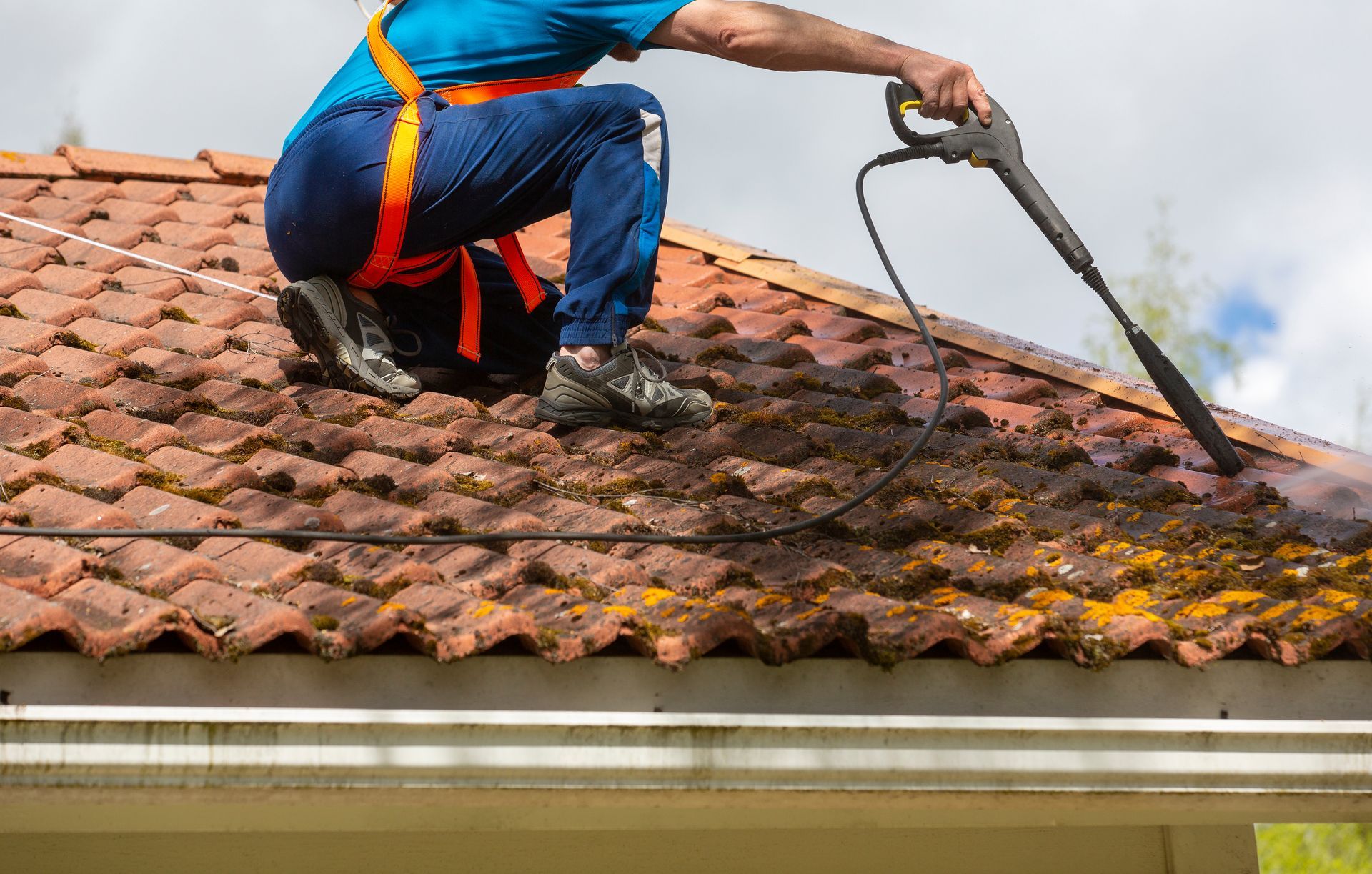 Worker pressure-washing a tiled roof with a hose and wand