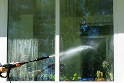 Person spraying a window with a hose, washing glass panes and water streaming down