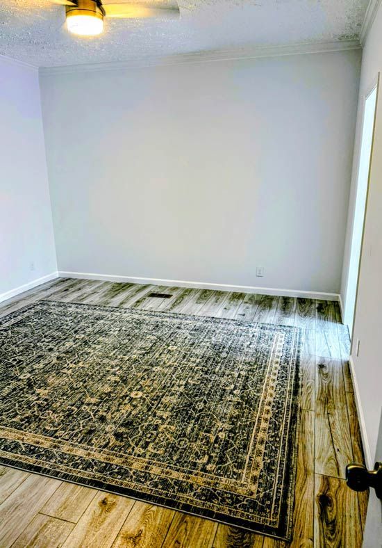 Empty room with white walls, ceiling fan, and large patterned rug on the floor